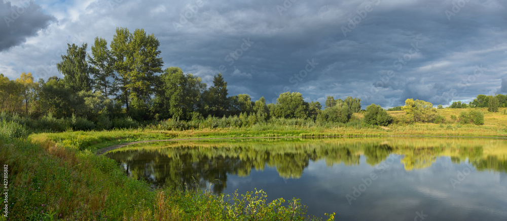 Stormy dramatic sky over the calm lake and green hills during sunset. Stormy dramatic sky over the calm lake and green hills during sunset.