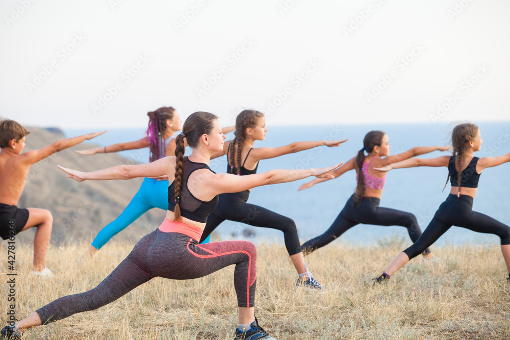 Fototapeta premium Instructor trains yoga kids in the mountains on the ocean.