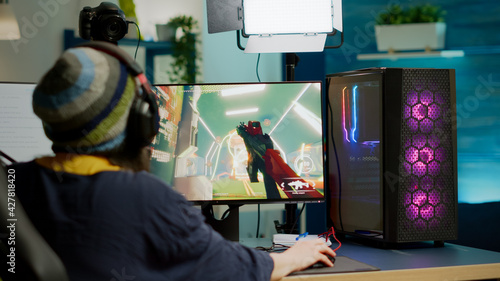 Fotografie Back shot of pro streamer with headphone playing FPS videogame during esport competition using RGB powerful computer