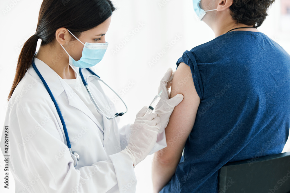 a nurse injects a vaccine into the shoulder of a patient wearing a medical mask a nurse injects a vaccine into the shoulder of a patient wearing a medical mask