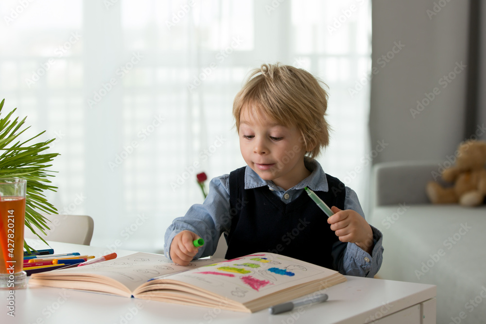 Cute preschool child, blond boy, filling some homework in a book and coloring pictures Cute preschool child, blond boy, filling some homework in a book and coloring pictures
