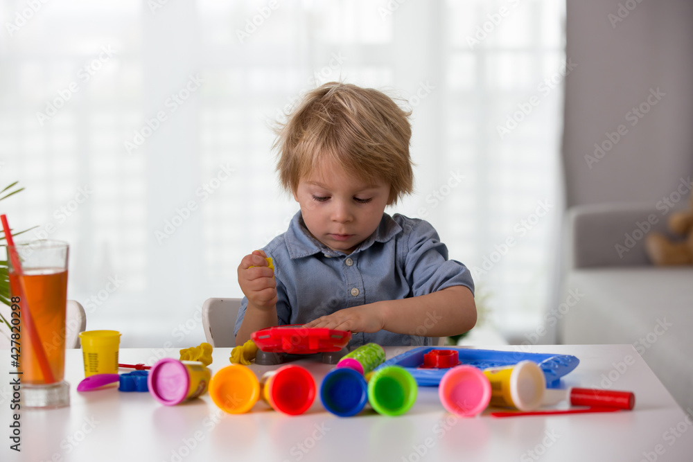 Cute blond child, boy, playing with play doh modeline at home, making different objects Cute blond child, boy, playing with play doh modeline at home, making different objects
