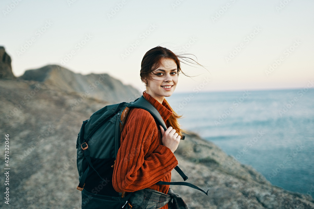 beautiful model with a backpack on her back in the mountains in nature near the sea and high rocks beautiful model with a backpack on her back in the mountains in nature near the sea and high rocks