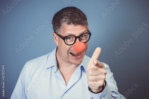 business man with blue shirt and black glasses and red clown nose posing in front of blue background in the studio