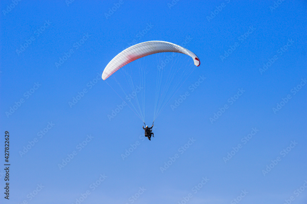 Tourist flying on a paraglider flying in the blue sky on a bight day. The sportsman paragliding. Tourist flying on a paraglider flying in the blue sky on a bight day. The sportsman paragliding.