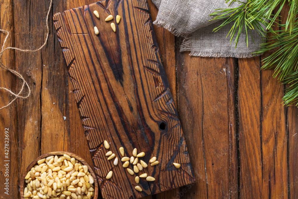 Obraz premium Still life cutting board on the table, a round bowl with pine nuts, linen cloth and a pine branch.