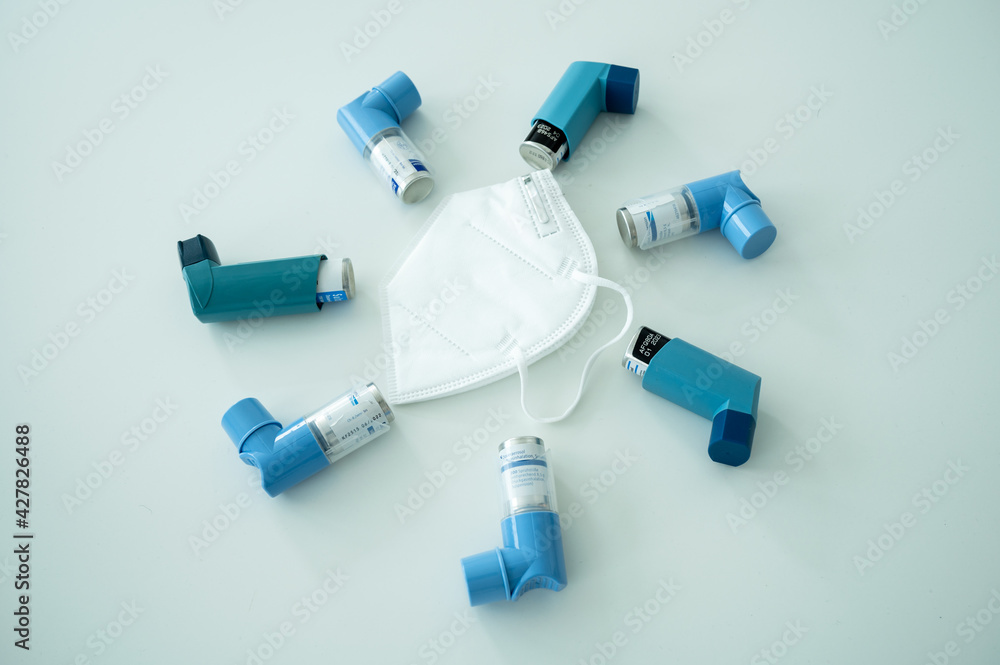 Various asthma spray inhalers and a Covid19 respirator mask on a white