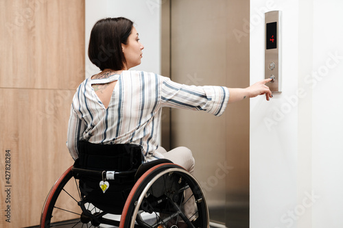 White young woman pushing button while sitting in wheelchair by elevator photo