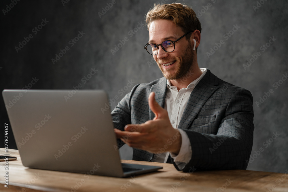 The smiling man talking by video call on a laptop while sitting at a table in the studio The smiling man talking by video call on a laptop while sitting at a table in the studio