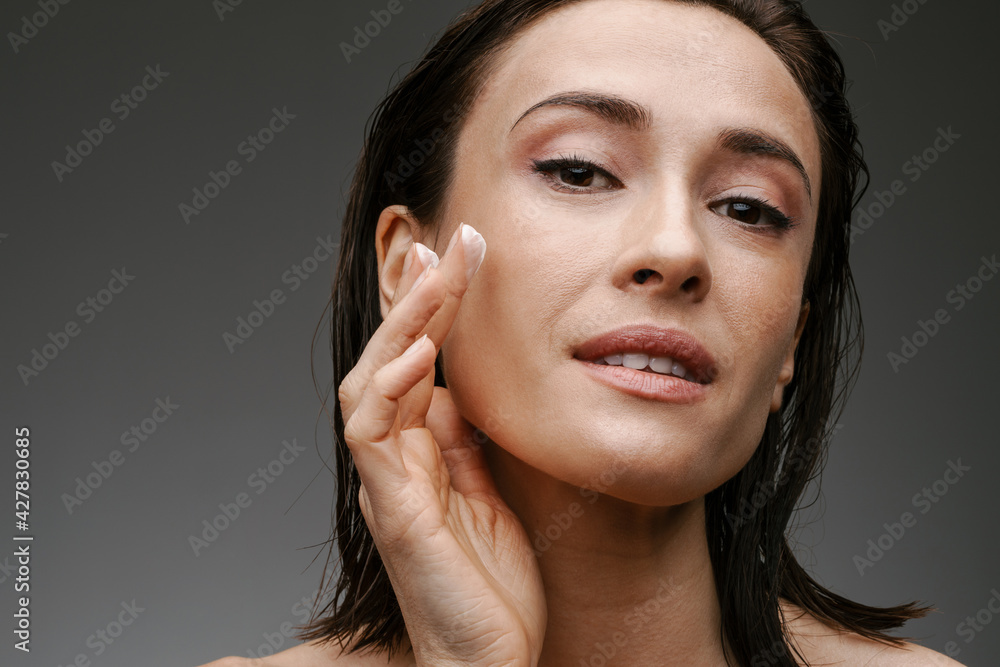 Half-naked woman looking at camera while applying facial cream Half-naked woman looking at camera while applying facial cream