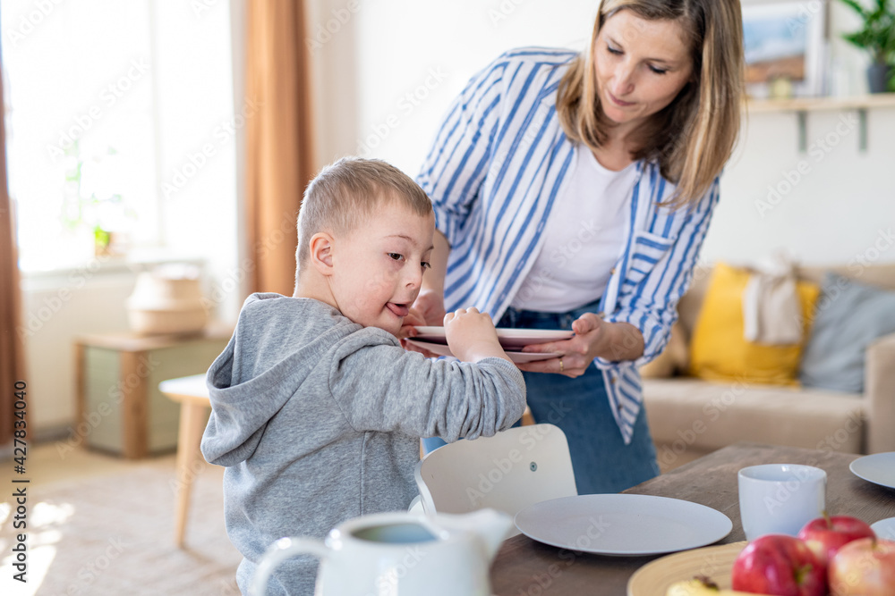 Single mother setting table for breakfast with down syndrome child at home.