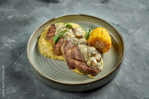 An appetizing dish - beef tongue steak with mushroom sauce, garnished with corn polenta in a plate. Gray background