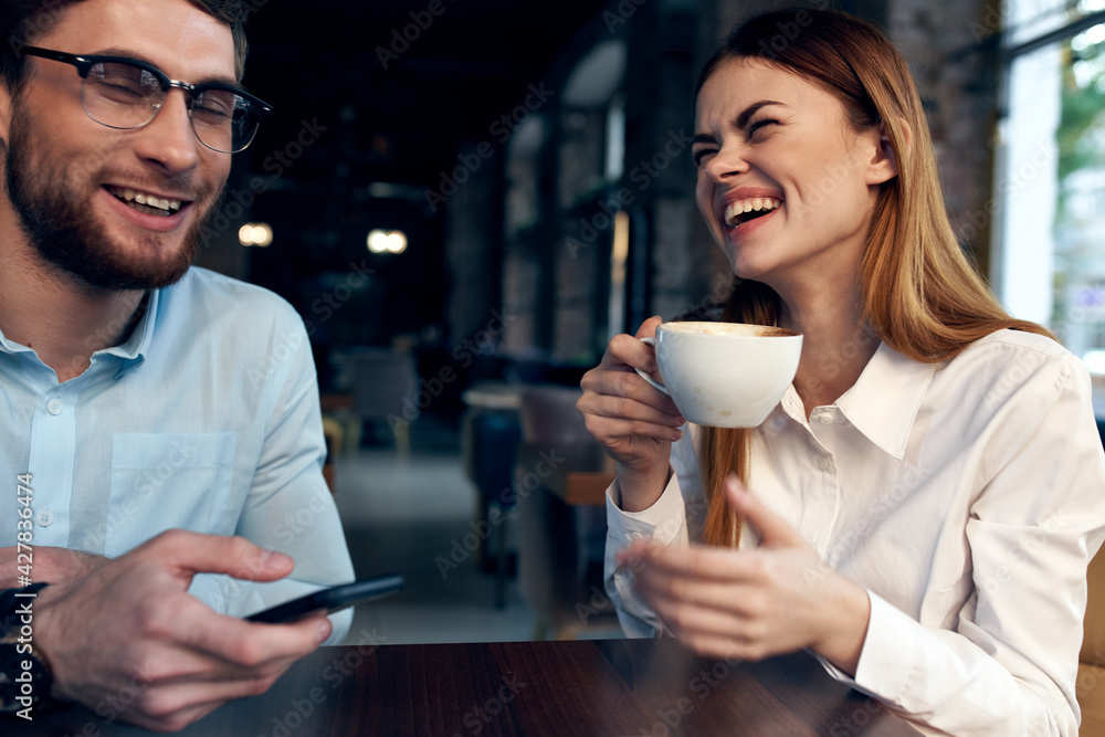 woman drinking coffee at the table next to a man work colleague technology