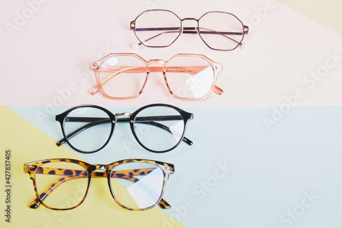 multiple eyeglasses on a multicolored background of pastel colors, geometric background, pink yellow and light blue colors, trendy eyeglass frames