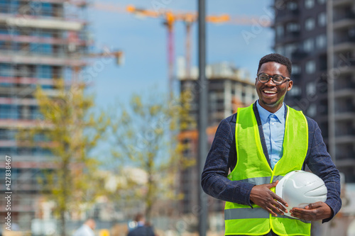 Portrait of a happy construction worker at a building site.  Front view of smiling architect in helmet. Confident architect standing at construction site. Overseeing the building process