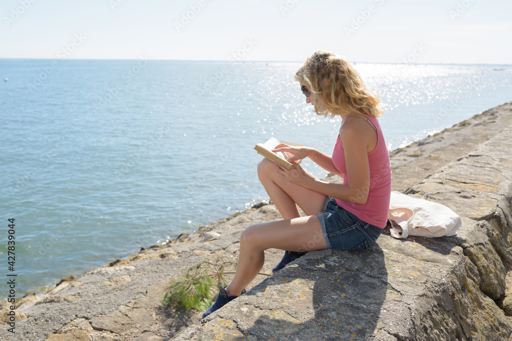 young woman reading book by the sea