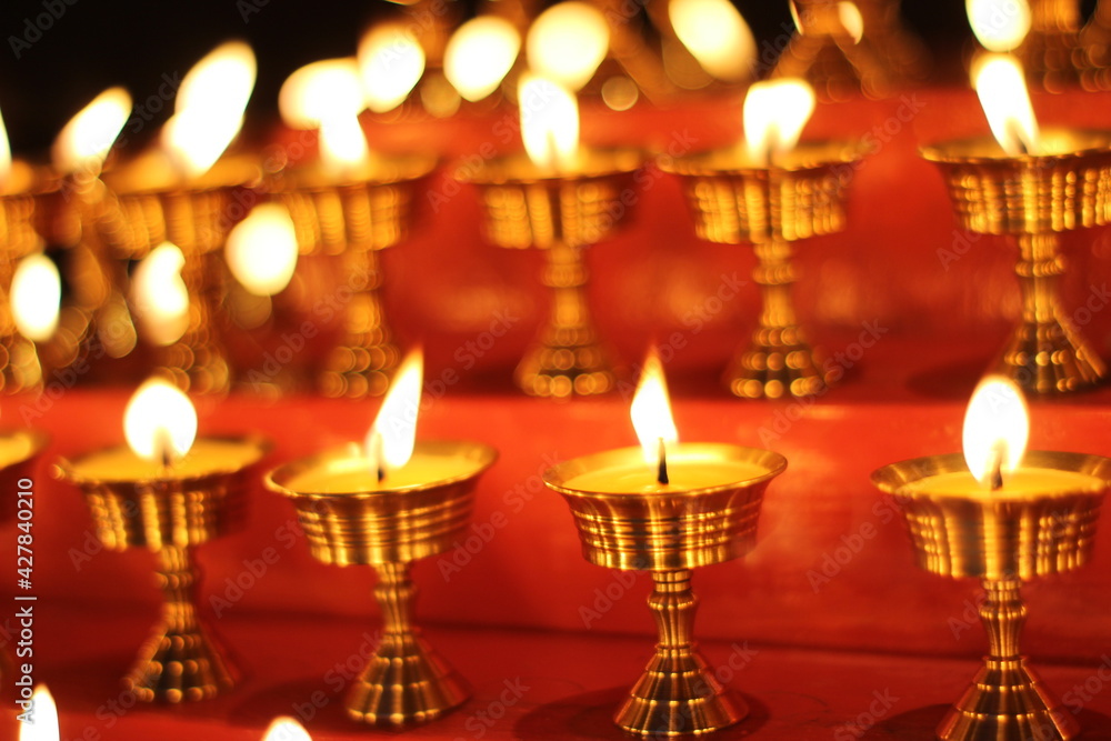Fototapeta premium Buddhist Altar Candles at Religious 108 Butter Lamp Festival in Temple Monastery. Beautiful Tranquil Scenic View of Oil Lamps and Swaying Flame for Praying