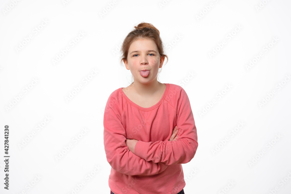 Portrait of offended young girl holding hands crossed and showing tongue, looking at camera Portrait of offended young girl holding hands crossed and showing tongue, looking at camera