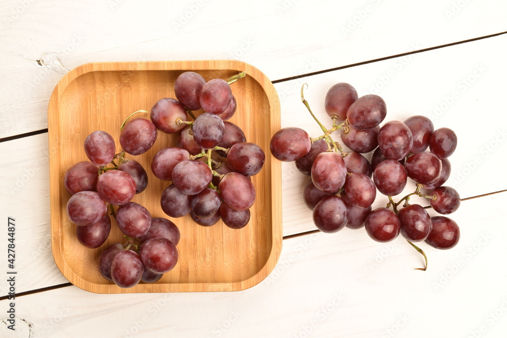 Two bunches of fresh organic, juicy, ripe, sweet grapes with a bamboo tray, close-up, on a painted table made of wood. Two bunches of fresh organic, juicy, ripe, sweet grapes with a bamboo tray, close-up, on a painted table made of wood.