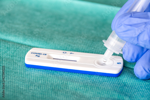 Close up of health care worker wearing blue surgical gloves and placing the sample in the covid-19 antigen diagnostic drug on a green surgical fabric 