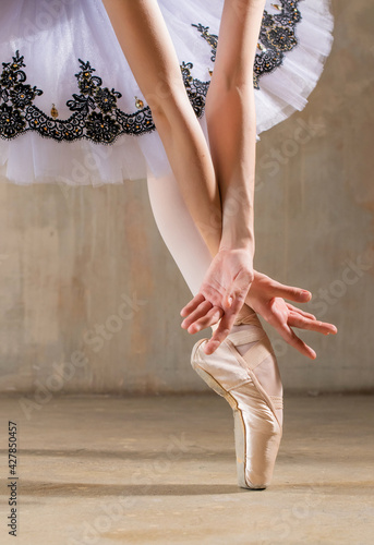 Leg in pointe under tutu and ballerina's hands on background of beige wall