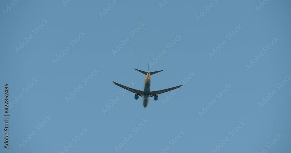 The plane flying away into the distance against the blue sky. Rear view of the airplane taking off from the airport. The plane flying away into the distance against the blue sky. Rear view of the airplane taking off from the airport.
