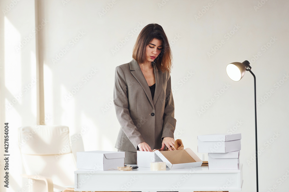 Packaging orders into the white boxes. Young woman in formal clothes is indoors. Conception of style Packaging orders into the white boxes. Young woman in formal clothes is indoors. Conception of style