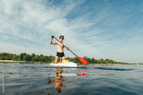 Athletic man paddles while sitting on a sup board floats on a pond. Surfing on the river on a sup board