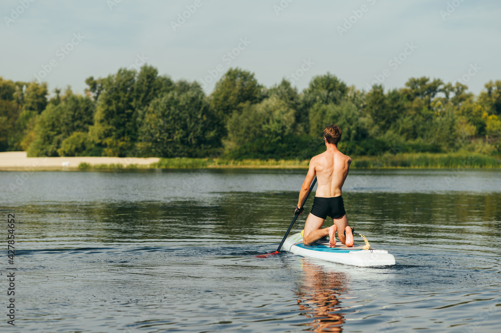 Man on a weekend walking on the river on a sup board on a background of beautiful landscape, view from the back. Man on a weekend walking on the river on a sup board on a background of beautiful landscape, view from the back.