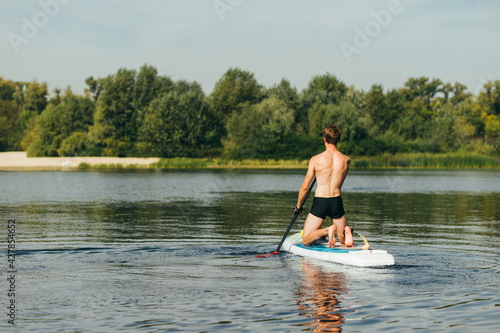 Man on a weekend walking on the river on a sup board on a background of beautiful landscape, view from the back.