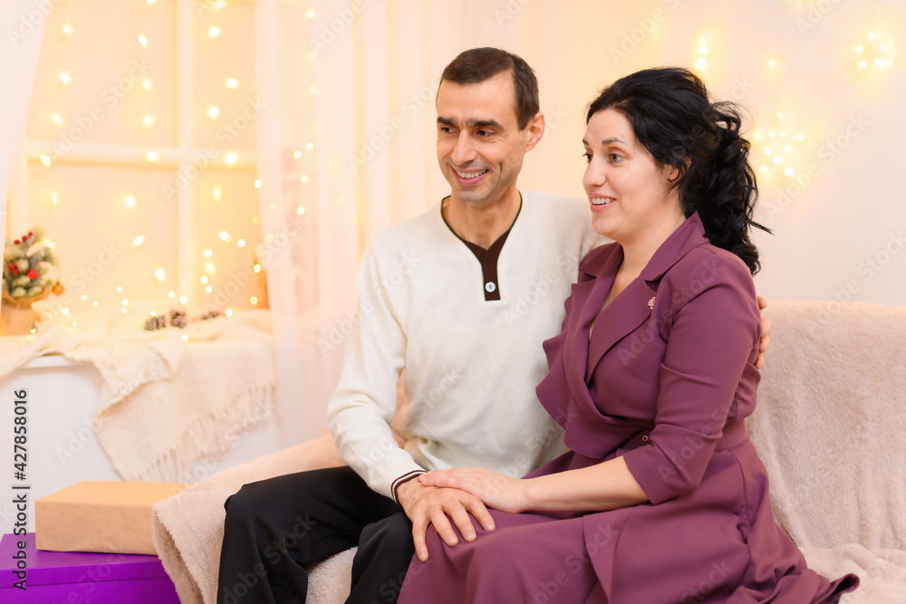 portrait of adult romantic couple sitting on a couch in home interior decorated with lights portrait of adult romantic couple sitting on a couch in home interior decorated with lights