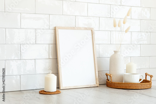 Blank picture frame mockup  rattan tray with cup of coffee  vase of dried flowers  candles. Brick tiles wall on background. Modern Scandinavian style interior.