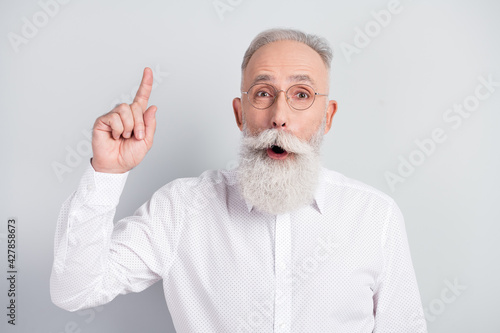 Portrait of handsome impressed grey hair old man point up wear spectacles white shirt isolated on grey color background