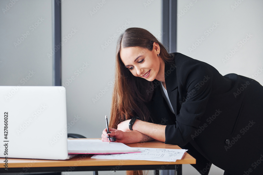 With laptop. Young adult woman in formal clothes is indoors in the office With laptop. Young adult woman in formal clothes is indoors in the office