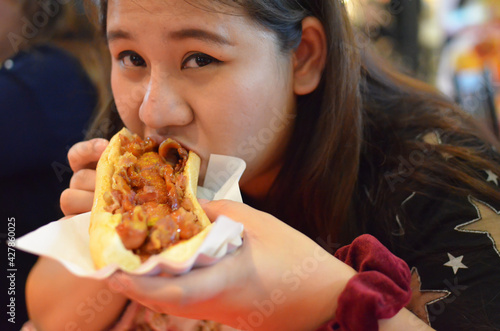 Young Asian woman eating sausage or hotdog burger