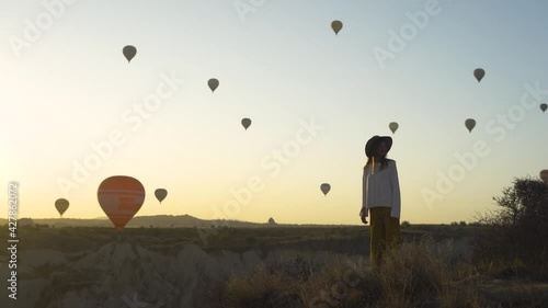 Woman watching the sunrise and hot air balloons taking off over valley in Cappadocia, Goreme, Turkey. 