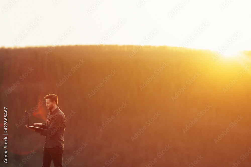 Fototapeta premium Man working outdoors with laptop in high mountains at sunset. He combines rest with work.