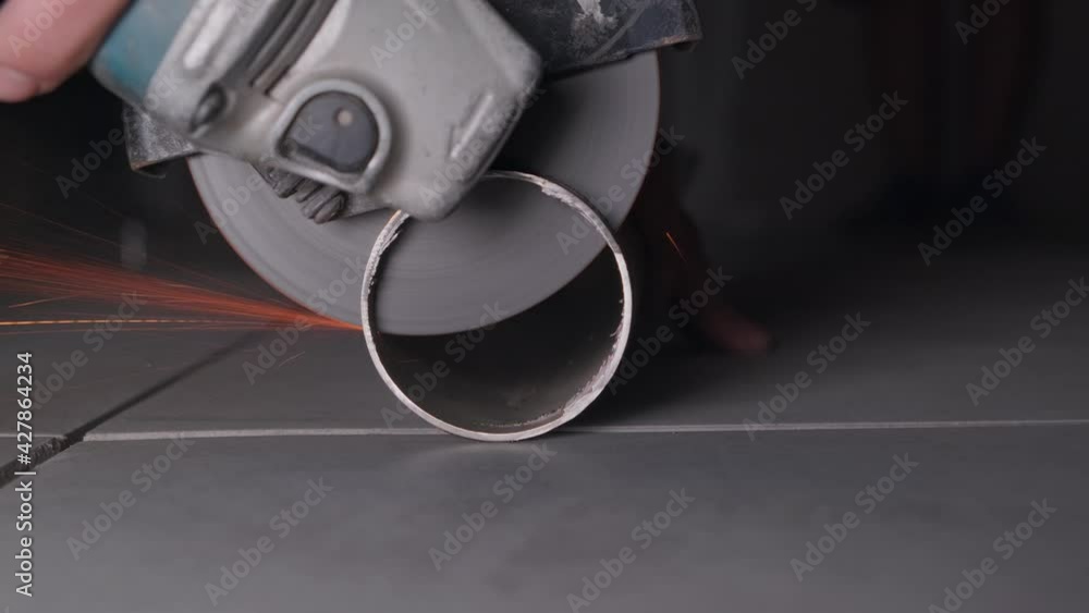 The foreman without gloves uses an angle grinder and cuts the stainless steel pipe. The engineer works and grinds with a grinding machine . Glowing bright sparks fly close up The foreman without gloves uses an angle grinder and cuts the stainless steel pipe. The engineer works and grinds with a grinding machine . Glowing bright sparks fly close up