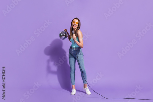 Full size photo of young cheerful smiling excited girl singing in karaoke hold disco ball isolated on violet color background