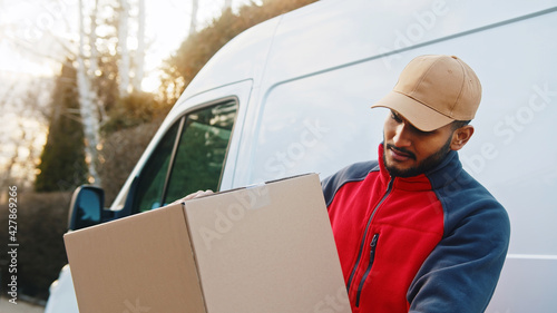 Delivery man holding parcel in front of transportation van. High quality photo © CameraCraft