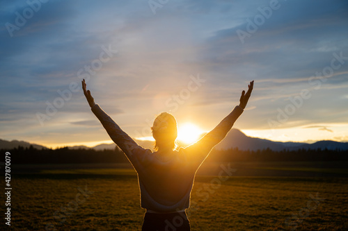 Woman embracing life standing outside in beautiful meadow with her arms raised h Fototapet