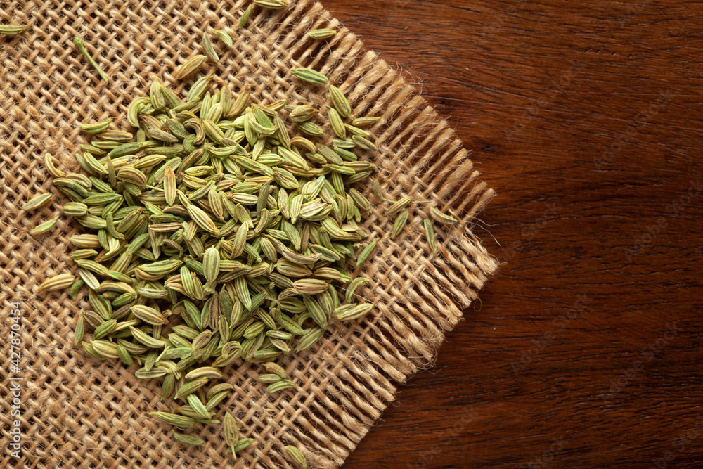 Macro close-up of Organic Fennel Seeds (Foeniculum vulgare) Badi sonf on the wooden top background and jute mat. Pile of Indian Aromatic Spice. Top view Macro close-up of Organic Fennel Seeds (Foeniculum vulgare) Badi sonf on the wooden top background and jute mat. Pile of Indian Aromatic Spice. Top view