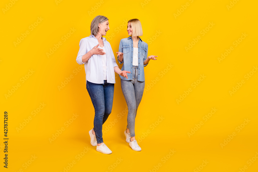 Full length body size photo mother and daughter talking walking together isolated bright yellow color background Full length body size photo mother and daughter talking walking together isolated bright yellow color background