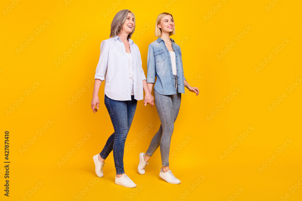 Full length body size photo mother and daughter holding hands going forward looking copyspace isolated bright yellow color background