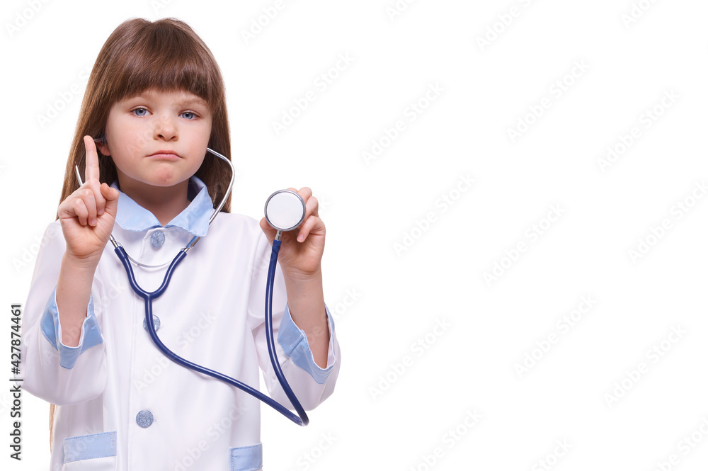 Cute serious little girl doctor wearing white coat holds stethoscope and shows finger gesture on white isolated background Cute serious little girl doctor wearing white coat holds stethoscope and shows finger gesture on white isolated background