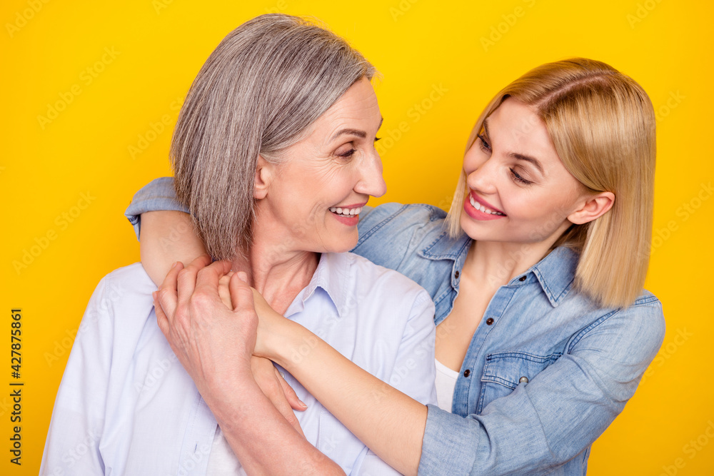 Photo portrait of mother and daughter embracing looking on each other holding hands isolated vibrant yellow color background Photo portrait of mother and daughter embracing looking on each other holding hands isolated vibrant yellow color background