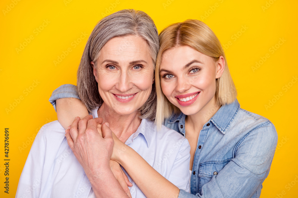Photo portrait of mother and daughter embracing together smiling holding hands isolated vivid yellow color background Photo portrait of mother and daughter embracing together smiling holding hands isolated vivid yellow color background