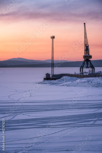 Port crane on the shore of the Gulf of White Sea. Sunset on the White Sea in winter.