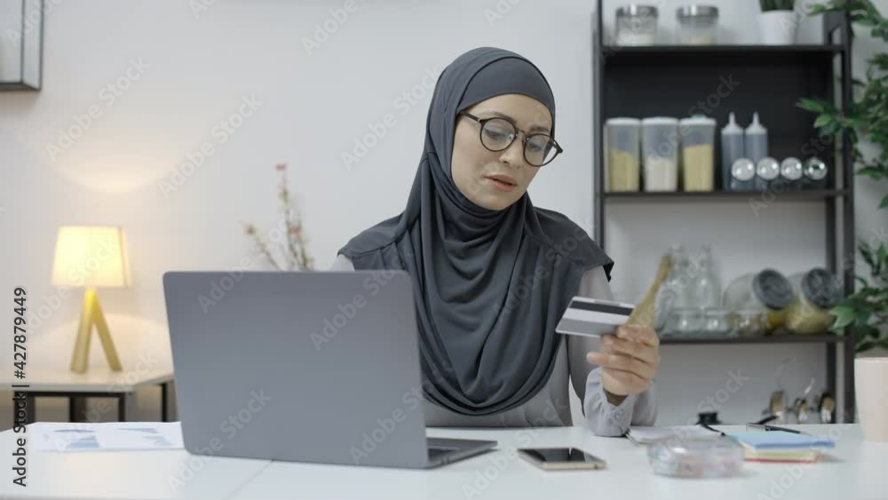 Smiling muslim female entering credit card number on laptop, shopping online Smiling muslim female entering credit card number on laptop, shopping online