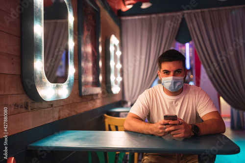 Chico guapo joven tomando cerveza y usando el smartphone en un pub decorado de tematica circense photo